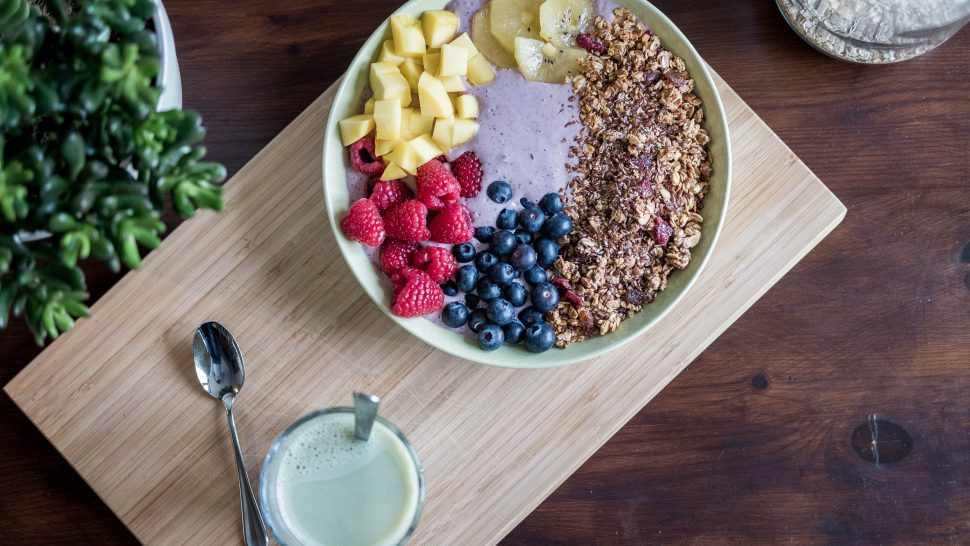 A bowl of granola and fruit and a pot of yoghurt on a wooden placemat